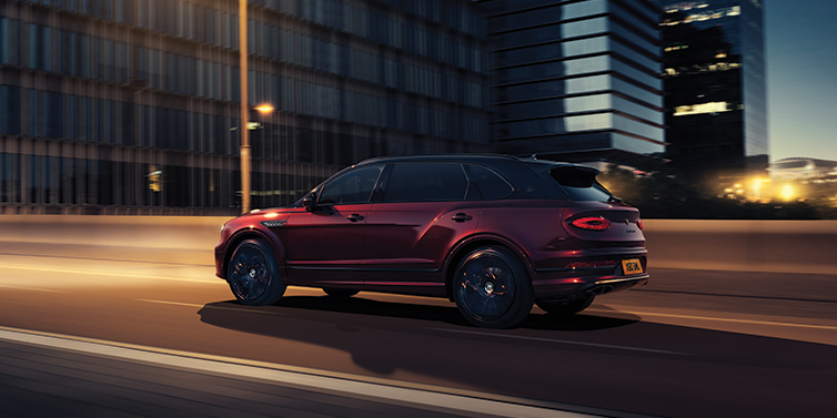 Bentley Lima Bentley Bentayga Extended Wheelbase Mulliner SUV in Cricket Ball red paint driving dynamically in city at night
